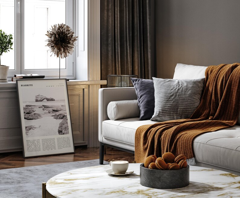 Pu&ograve; includere: Un soggiorno con un divano bianco, cuscini e una coperta color ruggine. &Egrave; visibile una stampa in bianco e nero di una scena costiera. Un tavolino con una ciotola di biscotti e una tazza di caff&egrave;.