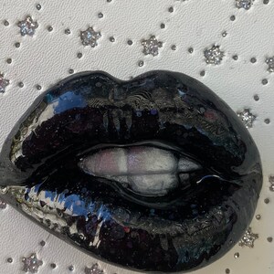 May include: Black glossy lips with a white, slightly open mouth. The lips are made of resin and have a shiny finish.