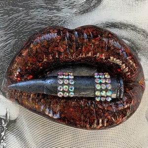 May include: A pair of red glitter lips with a black bullet with rhinestones in the middle of the lips.