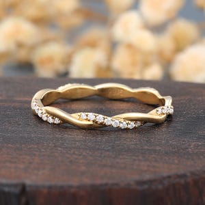 May include: A gold ring featuring a twisted band design. One half of the twisted metal strand is set with a row of small, clear, round-cut stones, while the other half of the band consists of smooth, polished gold metal with a reflective surface.
