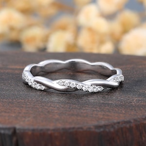 Könnte beinhalten: Ein Ring aus silberfarbenem Metall mit einem gedrehten, seilartigen Banddesign. Eine Hälfte des gedrehten Bandes ist mit kleinen, klaren, rund geschliffenen Steinen besetzt, während die andere Hälfte aus einer glatten, polierten Metalloberfläche besteht.