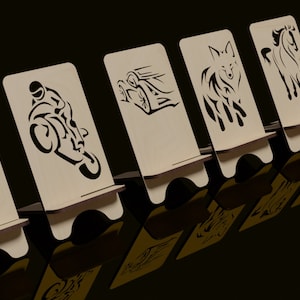 May include: Five wooden phone stands with different designs. The designs include a cat, a motorcycle, a car, a wolf, and a horse. The stands are all made of light brown wood and have a black background.