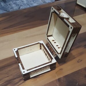以下が含まれることがあります： ヒンジ付きの蓋が付いた木製の箱。箱は開いており、中は空です。箱の前面と側面には装飾的なデザインが施されています。