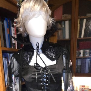 May include: Black gothic-style outfit on a mannequin. The ensemble includes a satin crop top with a lace-up front, a pleated skirt, and sheer sleeves adorned with butterfly patterns. A black choker and headpiece complete the look.