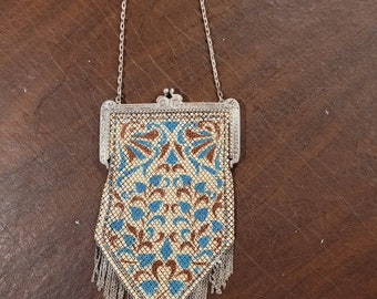 May include: A silver mesh purse with a chain strap and a blue and brown floral pattern. The purse has a fringe detail at the bottom.