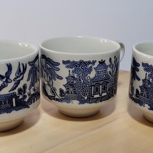 Puede incluir: Tres tazas de té blancas con un patrón de sauce azul y blanco. Las tazas tienen un diseño clásico con un patrón floral azul y blanco.