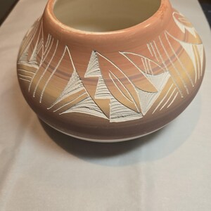May include: A round ceramic pot with a wide opening, featuring a warm, earthy colour palette. The pot has shades of brown, orange, and cream. Intricate white geometric designs are carved into the surface, adding texture. Likely for decorative use, the pot is a handcrafted item.
