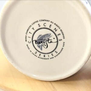 May include: Off-white ceramic mug with a circular logo featuring a fish illustration and the word "Barista." The logo is surrounded by text that reads "City Scenes Series" and "Made in China." The mug is microwave and dishwasher safe.