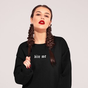 May include: Black sweatshirt with the text "bite me" in white gothic font.