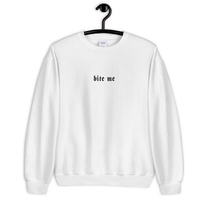 May include: White sweatshirt with the phrase "bite me" printed in black gothic font. The crew neck sweatshirt is hanging on a black hanger. The Gildan brand logo is visible on the tag.