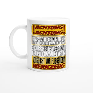 Könnte beinhalten: Weiße Keramiktasse mit gelbem und rotem Design. Der Text auf der Tasse lautet "!ACHTUNG! !ACHTUNG! KFZ-MECHANIKER BEI DER ARBEIT SICHERHEITSABSTAND EINHALTEN VORSICHT VOR FLIEGENDEM WERKZEUG"