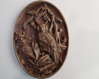 May include: Oval wooden wall art featuring a detailed relief carving of an owl perched on books, with branches and foliage. The artwork is in shades of brown and has a rustic, natural aesthetic. The owl is the focal point, with intricate feather details.