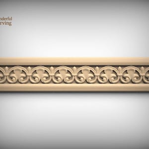 May include: A rectangular light-colored wooden molding strip featuring a continuous carved relief pattern of repeating scrolls and fleur-de-lis motifs. The piece has a smooth, beveled frame border and a natural wood grain finish throughout the design.