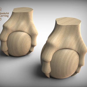 Op de afbeelding: Twee houten, gesneden meubelpoten, elk met een handachtig ontwerp dat een bal vasthoudt. De poten zijn gemaakt van lichtgekleurd hout en hebben een gladde afwerking. Het logo "Wonderful Carving" is linksboven zichtbaar.