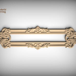 May include: A light tan, horizontal wooden molding piece featuring intricate, symmetrical scrollwork and acanthus leaf carvings on both ends and the center. The rectangular frame design includes a smooth, open central space for decorative application.