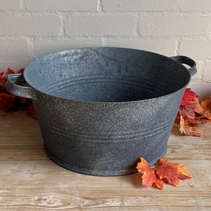 May include: A grey metal tub with two handles. The tub has a speckled finish and is sitting on a wooden surface.