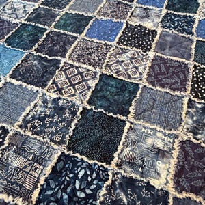 May include: A handmade quilt featuring a patchwork design with various shades of blue and white fabrics. The squares are arranged in a grid pattern, with frayed edges adding texture. The quilt showcases a mix of patterns, including floral, geometric, and abstract designs.