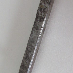 May include: A long, thin, metal bar with three holes and two brass screws. The bar is slightly rusted and has a textured surface.