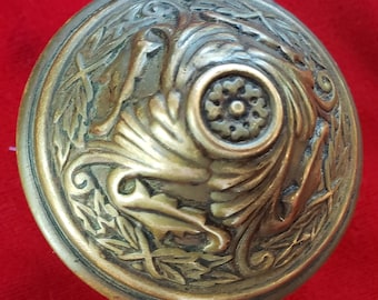 Può includere: Una maniglia per porta in ottone con un design ornamentale che presenta una rosetta centrale e un motivo floreale a spirale.