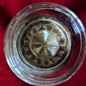 Könnte beinhalten: Nahaufnahme eines durchsichtigen Glasflaschenverschlusses mit einem sternförmigen Design in der Mitte. Der Verschluss hat einen erhabenen, strukturierten Rand.