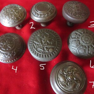 Puede incluir: Siete pomos de puerta antiguos con diseños intrincados. Los pomos son de metal y tienen un acabado marrón oscuro. Todos tienen formas y tamaños diferentes, pero todos tienen un estilo ornamentado similar.