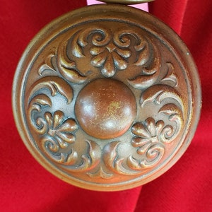 May include: A vintage-style door knob with a decorative, ornate design. The knob is made of brass and has a dark brown finish. The design features intricate floral patterns and swirls.