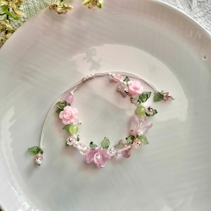 May include: A delicate bracelet with pink and green floral accents. The bracelet is made with small beads and features a butterfly charm.