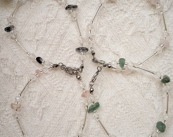 May include: Three silver anklets with clear beads and different colored gemstone accents. The anklets are on a white fabric background.