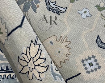 Könnte beinhalten: Aufgerollter beigefarbener Teppich mit einem detaillierten Blumen- und geometrischen Muster in Blau-, Grau- und Cremetönen. Der Teppich hat ein zentrales Blumenmotiv und sich wiederholende Bordürendesigns. Der Teppich besteht aus gewebtem Material.
