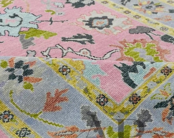 May include: Close-up of a pink and blue patterned rug with floral and geometric designs. The rug features a light pink central field with blue and yellow borders. The design includes green, gray, and orange accents.