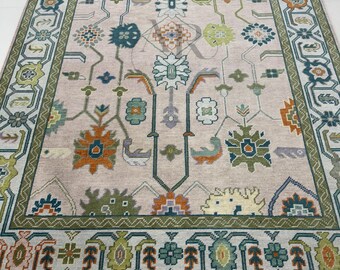 May include: A beige rug with a green, orange, and blue geometric pattern. The rug has a fringe border.
