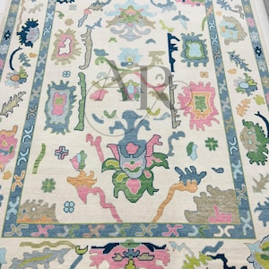 May include: A cream-colored rug with a floral pattern in shades of pink, blue, green, and yellow. The rug has a border with a repeating pattern of blue and white.