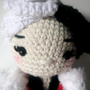 Puede incluir: Una mu&ntilde;eca de crochet con pelo de lana blanca, un gorro de crochet blanco y un atuendo de crochet negro y rojo.