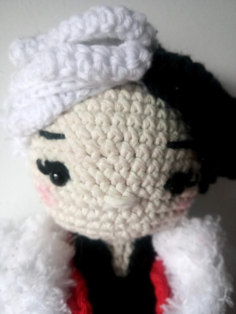 Puede incluir: Una mu&ntilde;eca de crochet con pelo de lana blanca, un gorro de crochet blanco y un atuendo de crochet negro y rojo.