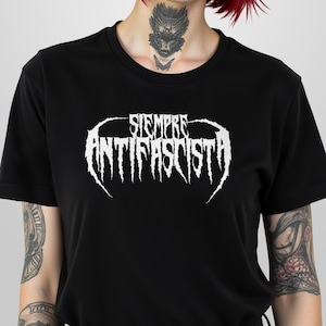 May include: Black crew neck t-shirt featuring the white text "SIEMPRE ANTIFASCISTA" in a gothic font. The shirt is made of a soft material and is suitable for casual wear. The design is centered on the chest.