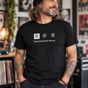 May include: A black short-sleeved t-shirt featuring a white graphic of three document alignment icons and the text "Radicalised by Basic Decency" printed in a white serif font across the centre of the chest area.