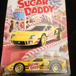 Puede incluir: Paquete de coche de juguete Matchbox con un Ford GT amarillo y negro, con la marca "Sugar Daddy". El embalaje tiene un tema de dulces, con "Sugar Daddy" en letras rojas grandes. Modelo en miniatura.