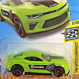 Può includere: Un'auto giocattolo Hot Wheels verde lime con dettagli neri e rossi. L'auto presenta il logo "Brembo" e "HW Speed Graphics" sulla confezione. La confezione è blu con il logo Hot Wheels.