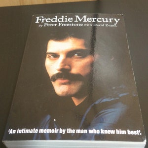 May include: A black and white book cover with a photo of Freddie Mercury. The title of the book is "Freddie Mercury" by Peter Freestone with David Evans. The text below the photo reads "An intimate memoir by the man who knew him best."