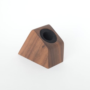 May include: A triangular wooden pen holder with a black foam insert. The holder is made of dark wood and has a smooth finish.