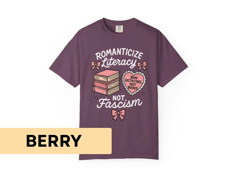 May include: Berry-colored t-shirt with a graphic design. The design includes the words "Romanticize Literacy, Not Fascism" with illustrations of books and a heart-shaped graphic. The shirt is made of a soft material.
