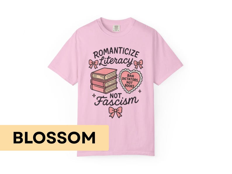 May include: A light pink t-shirt with the words "Romanticize Literacy Not Fascism" and a graphic of books and a heart. The shirt also has the word "Blossom" in a yellow rectangle at the bottom.