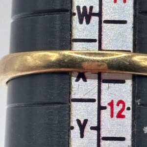May include: A gold ring band positioned on a black ring sizing mandrel. The ring rests between the size markings W and Y on the vertical scale, indicating a size that aligns with the 11 and 12 markers printed in red on the white measuring tool.
