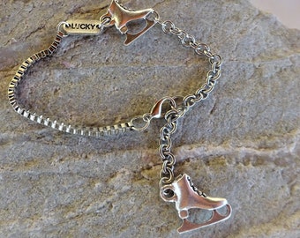 May include: Silver chain bracelet with two ice skate charms. The bracelet has a box chain and a lobster clasp. The charms are attached to the chain with jump rings. The bracelet has a "LUCKY" tag.