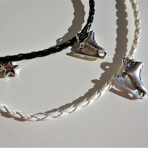May include: Two braided leather bracelets with silver charms. One bracelet is black and features a star charm. The other bracelet is white and features a silver ice skate charm.