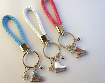 May include: Three keychains with braided leather straps in pink, white, and blue. Each keychain has a silver key ring with a charm of a silver ice skate with rhinestones.