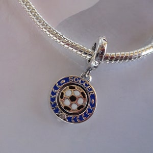 Op de afbeelding: Een zilveren armband met een blauwe en gouden voetbalbedel. De bedel heeft het woord "SOCCER" rond de rand.