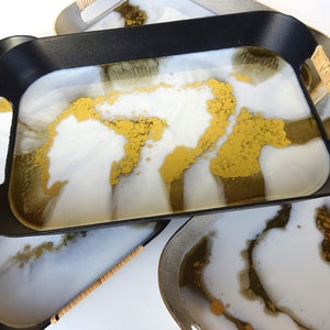 May include: Set of four black trays with natural woven handles. Each tray features a white and gold resin with a marbled design.