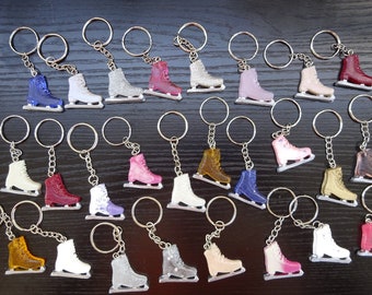 May include: A collection of 24 ice skate keychains in various colors, including white, pink, blue, red, gold, and silver. The keychains are made of resin and feature a detailed ice skate design.