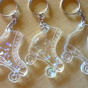 May include: Three clear acrylic roller skate keyrings with silver key rings. Each keychain features iridescent glitter embedded in the plastic.